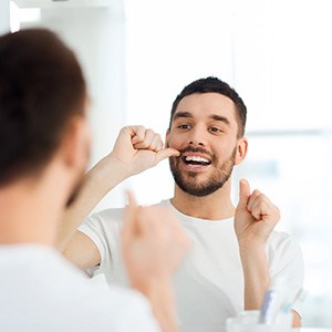 Man smiling while flossing in bathroom