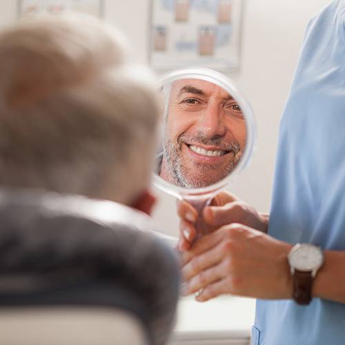 Man smiling at reflection in handheld mirror